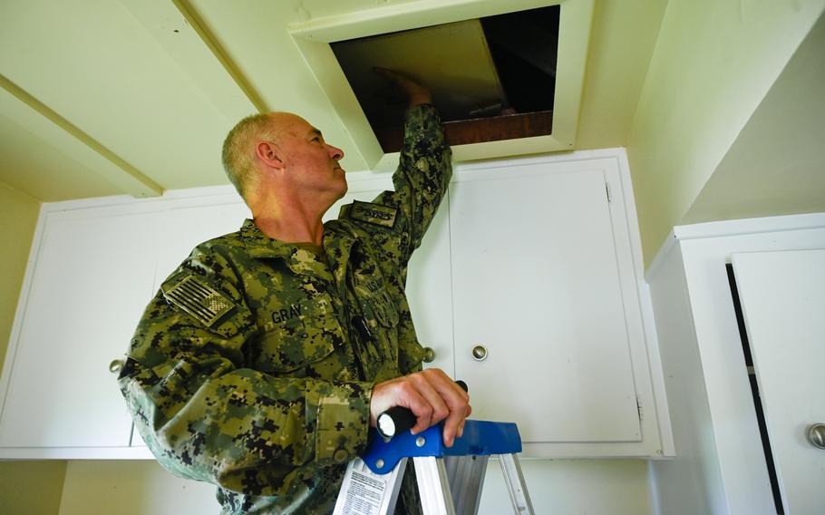 A man on a ladder moving a ceiling tile to do an inspection.