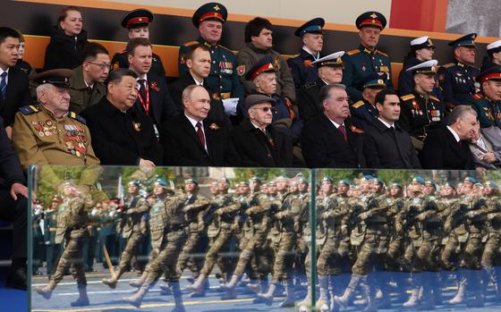 A row of foreign leaders, including Vladimir Putin and Xi Jinping, watch a parade of military personnel, who are seen reflected in the glass barrier where the dignitaries are seated.