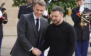 Emmanuel Macron and Volodymyr Zelenskyy smile as they shake hands.