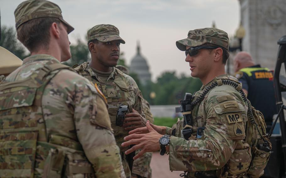 Three service members in uniform standing and talking with the U.S. Capitol in the background. 