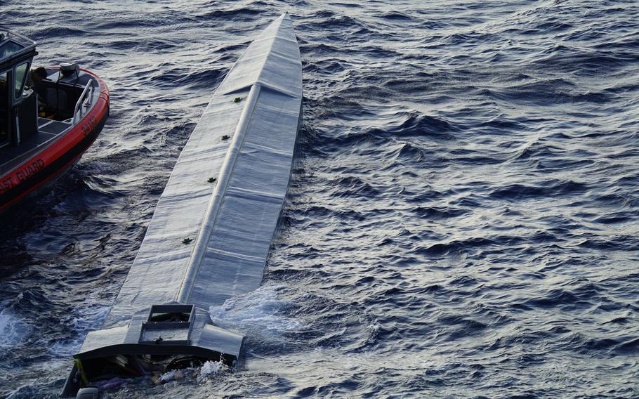 A boat, very low to the water, floats near a Coast Guard ship.