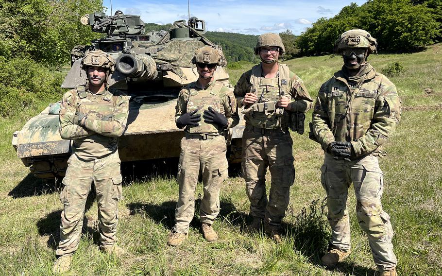 Four soldiers pose in front of a tank
