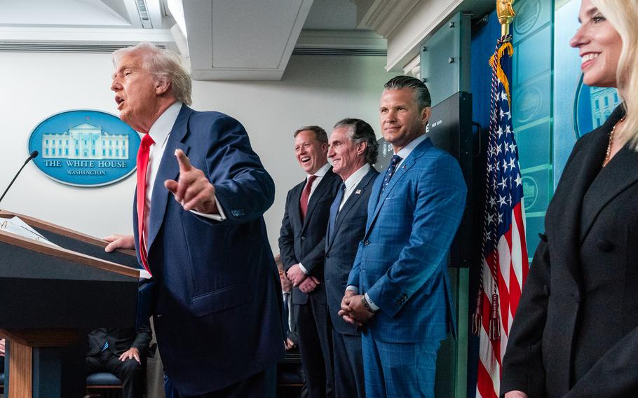 Donald Trump speaks into a microphone with top officials lined up behind him.