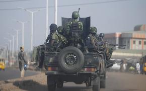 A modified pickup truck carrying soldiers with machine guns and rifles drives down a street.