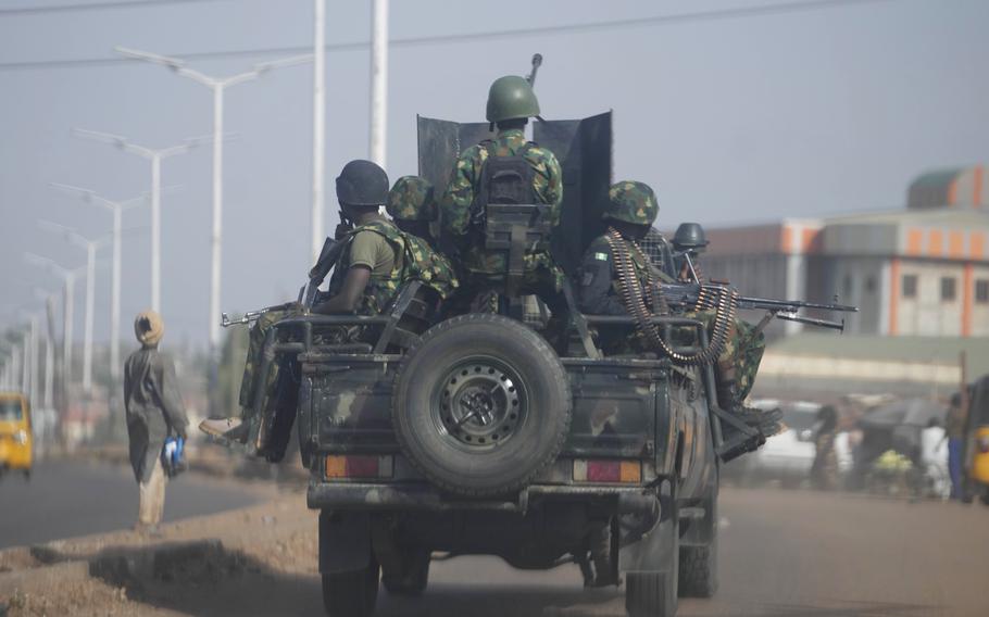 A modified pickup truck carrying soldiers with machine guns and rifles drives down a street.