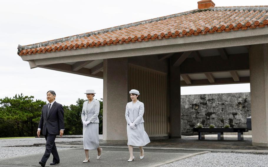 Three people in formal clothes, a man in a dark suit and two women in white, walk out of a mausoleum.
