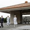 Three people in formal clothes, a man in a dark suit and two women in white, walk out of a mausoleum.