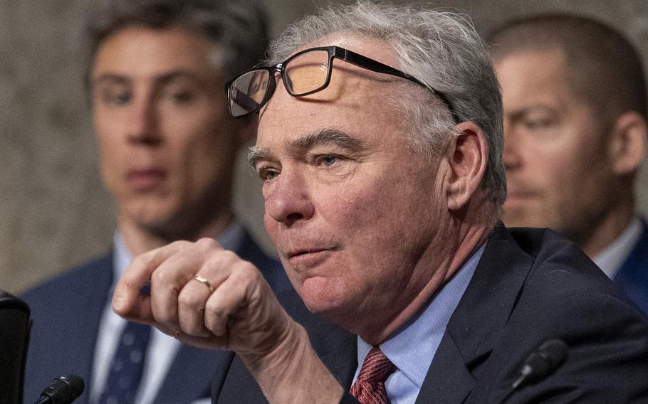 A close-up view of Tim Kaine, with his eyeglasses resting on his forehead, gesturing with his left hand as he speaks.
