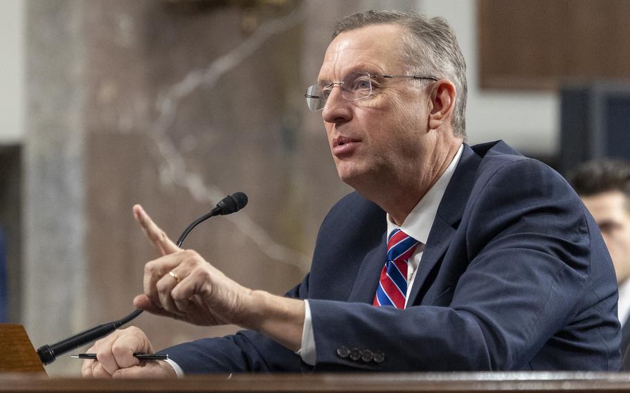 Collins is seated at a hearing, speaking and pointing.