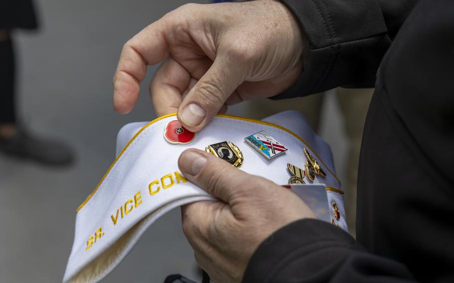 A pair of hands hold a white cap adorned with pins.