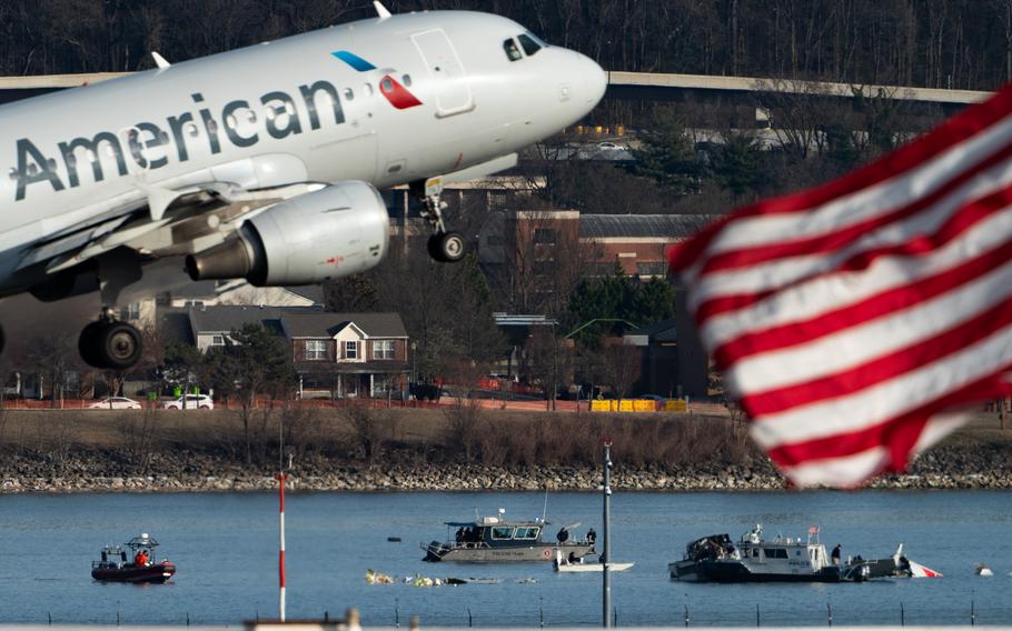 An American Airlines plane is airborne, a waving American flag flies in the foreground, the Potomac in the background.