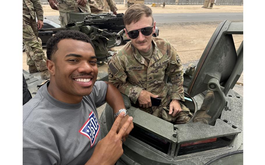 Two men pose for a photo in a military vehicle