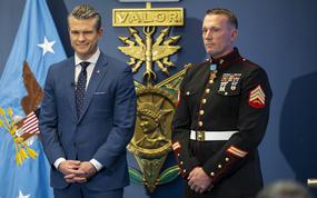 Hegseth in a suit and Meyer in uniform with a representation of the Medal of Honor, reading Valor, in the background.