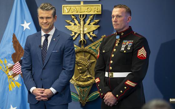 Hegseth in a suit and Meyer in uniform with a representation of the Medal of Honor, reading Valor, in the background.