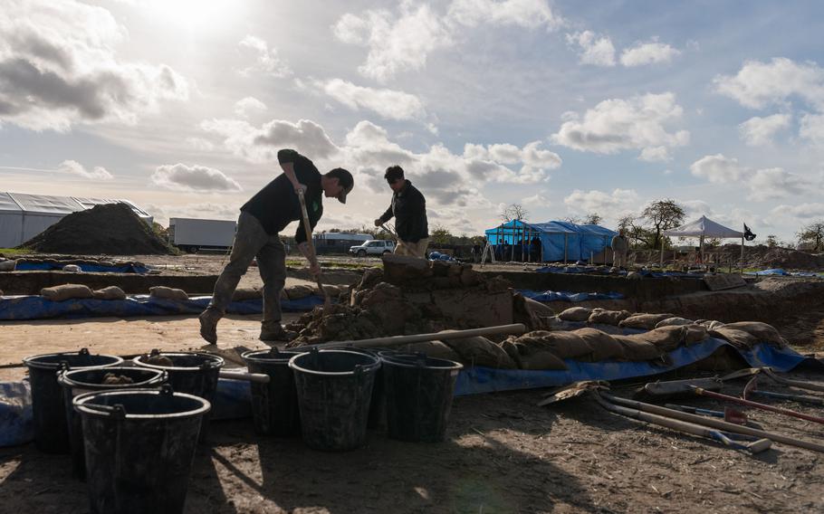 Army Cpl. Anthony Boulanger, left, and Army Spc. Alexis Jove, both with the 2nd Cavalry Regiment, shovel soil into buckets at an excavation site in Wistedt, Germany, Oct. 30, 2023. The soil will later be examined for airplane debris and potential human remains. 