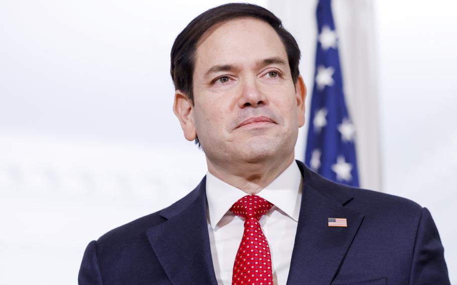 Close-up view of Marco Rubio in a dark suit and red tie standing in front of a U.S. flag.