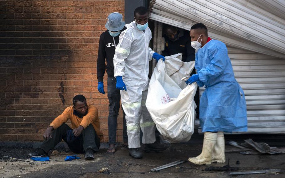 A family member watches on as police forensics officers carry the body his brother who was found inside a burned shop, in Johannesburg, South Africa, Sunday, July 11, 2021.