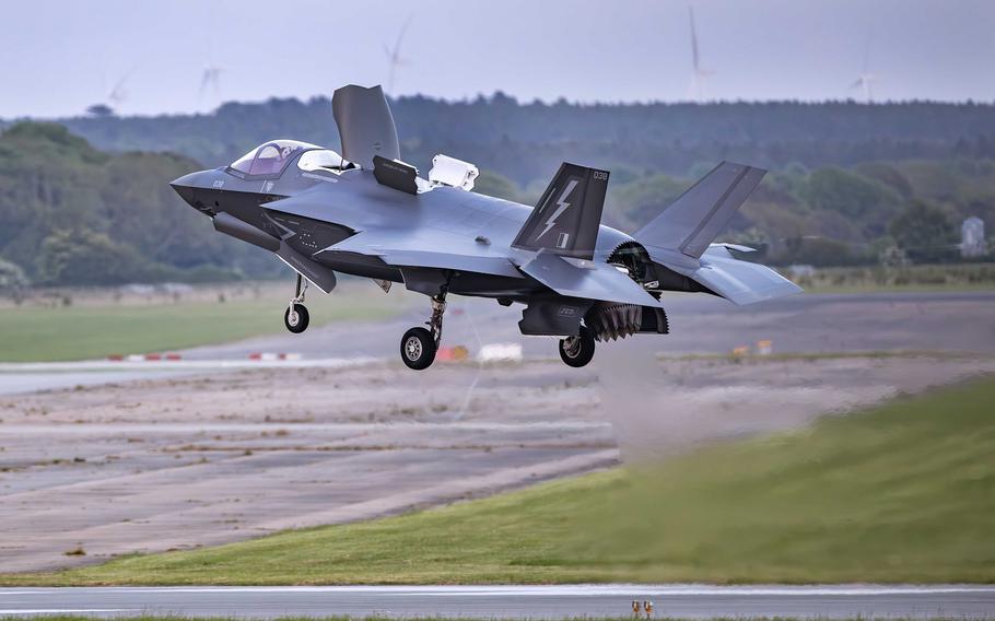 A grey F-35B Lightning II stealth fighter jet with marking “A” and “039” on the tail is shown during a landing approach with landing gear extended over a runway.