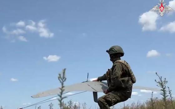 A Russian service man holds a slim, gray drone that he is orienting towards the sky.
