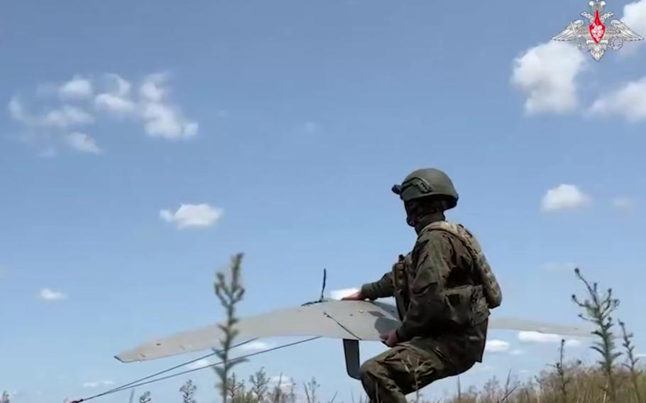 A Russian service man holds a slim, gray drone that he is orienting towards the sky.