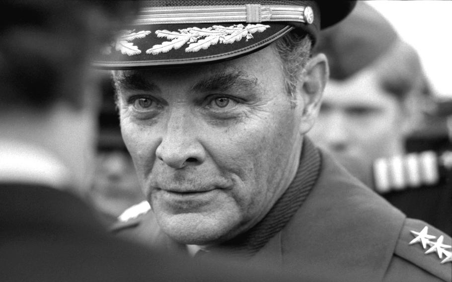 A black and white portrait of a man looking intently at another person whose out-of-focus head takes up the left side of the photo.