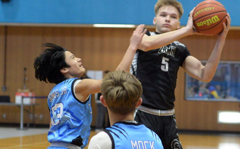 Zama's Joshua Norris goes up for the ball against Osan's R.J. Jones and Dimitri Mock. The Trojans won 59-26.