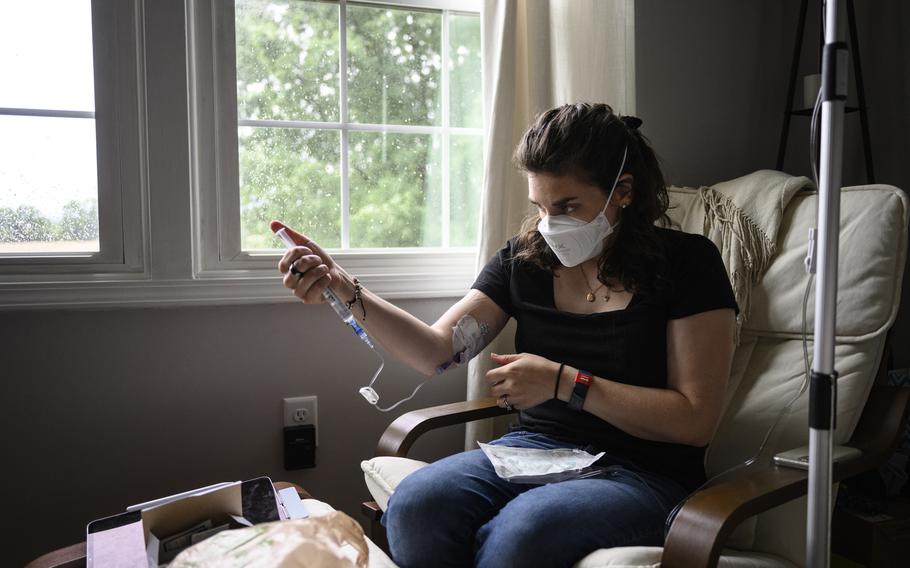 Mallory Stanislawczyk, who has long covid, gives herself a saline infusion through a peripherally inserted central catheter, or PICC, line. 