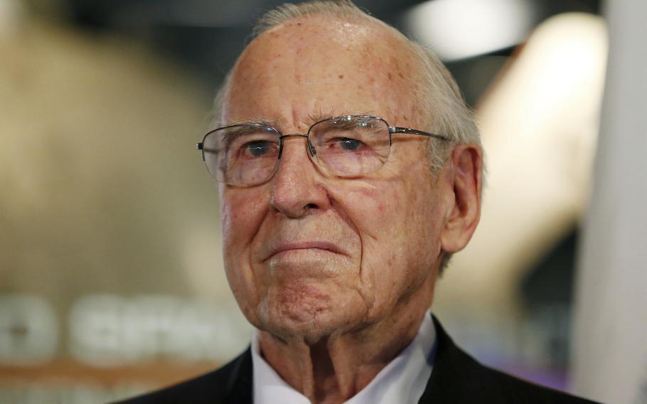 An elderly man wearing glasses, seen from the neck up, poses in front of a blurred background.