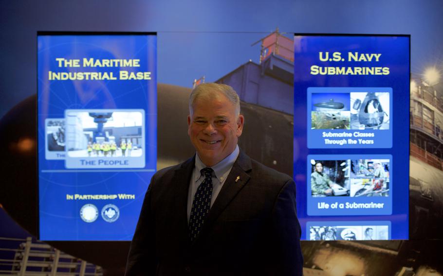 A man in a suit and tie smiles while standing between two vertical display screens.