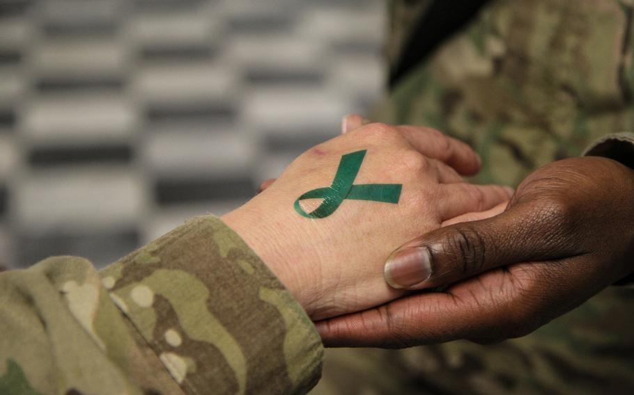 A soldier places a teal ribbon temporary tattoo on another soldier's hand. The teal ribbon is the symbol of sexual assault survivors and awareness. A new Government Accountability Office report found that the Defense Department needs to do a better job addressing the needs of service members who are victims of sexual assault, sexual harassment and domestic sexual abuse.