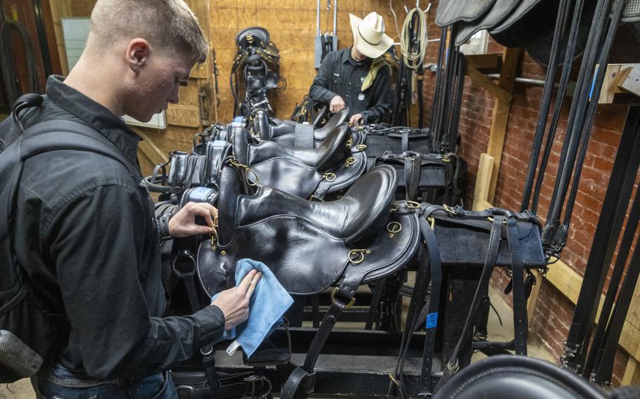 Soldiers clean a line of saddles.