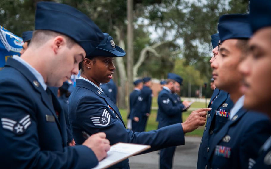 Airmen on the left take notes and inspect the airmen lined up on the right.