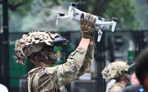 A soldier holds onto a gray drone.