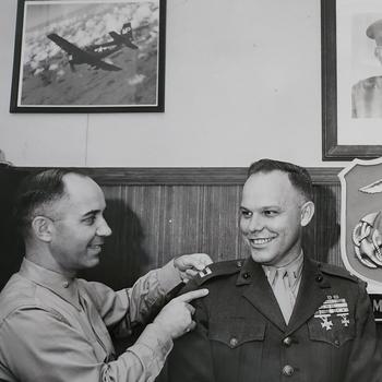 A Marine pins another Marine’s uniform, promoting him to captain