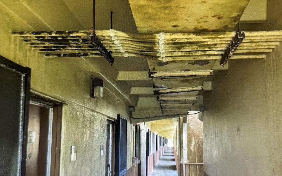 A long concrete corridor with a deteriorating ceiling showing exposed structural elements and water damage.