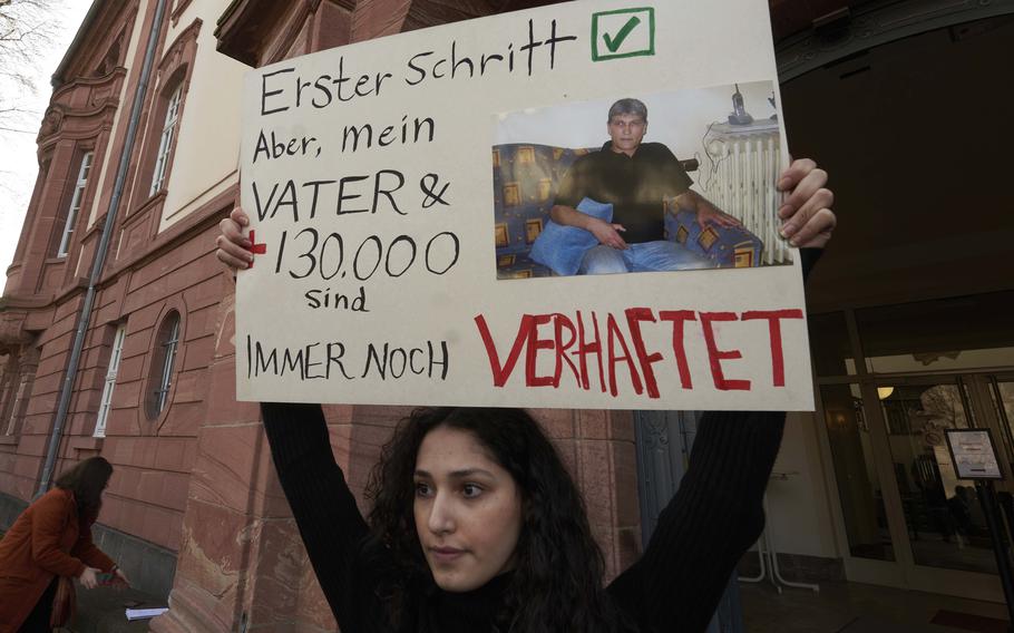 A woman holds a sign in front of the Higher Regional Court building in Koblenz, Germany, on Feb. 24, 2021. The Koblenz court is scheduled to deliver its ruling Thursday, Jan. 13, 2022, in the trial of Anwar Raslan, a former Syrian secret police officer who is accused of crimes against humanity for overseeing the abuse of detainees at a jail near Damascus a decade ago..