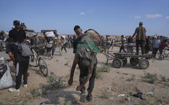 A man, seen from behind, carries the body of another man over his shoulder across sandy terrain.
