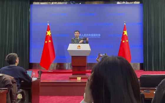 Senior Col. Wu Qian, the defense ministry's top spokesperson, holds up souvenir pins to mark the Chinese Air Force anniversary during a press conference in Beijing, Thursday, Nov. 30, 2023. China's defense ministry said Thursday that the U.S. should stop interfering in both Taiwan and the South China Sea, calling U.S. arms sales to Taiwan a powder keg that is making the situation more dangerous. 