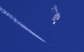 In this photo provided by Chad Fish, the remnants of a large balloon drift above the Atlantic Ocean, just off the coast of South Carolina, with a fighter jet and its contrail seen below it, Feb. 4, 2023. China said Tuesday, Feb. 7, 2023, it will “resolutely safeguard its legitimate rights and interests” over the shooting down of a suspected Chinese spy balloon by the United States, as relations between the two countries deteriorate further. (Chad Fish via AP, File)