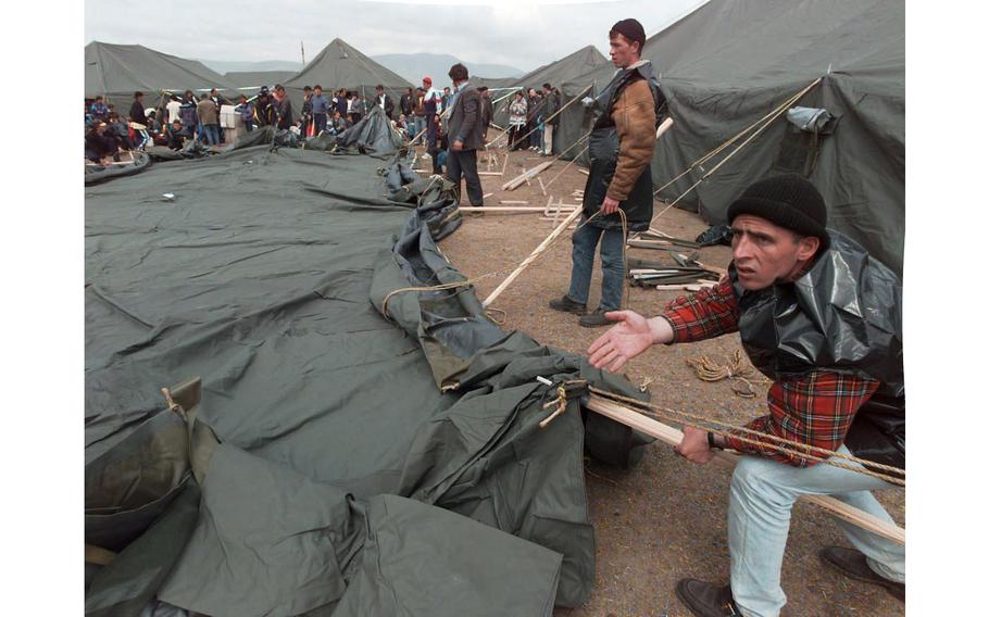Newly arrived Kosovo refugees put up a tent at the Brazda refugee camp. Scores of refugees are in the background waiting for these gentlemen to erect the tent so that they will have a place to live. 
