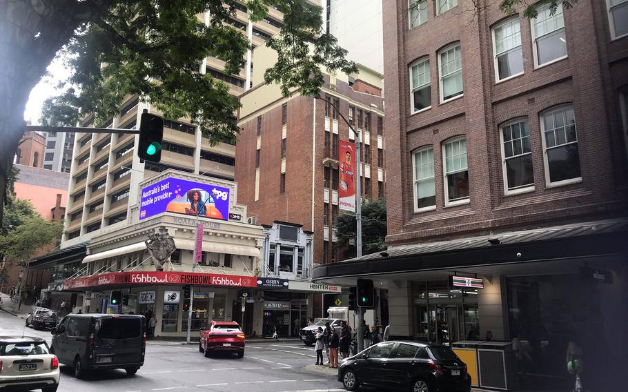 A city street corner in Brisbane, Australia, has brick buildings and some neon signs.