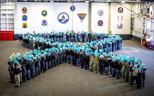 Sailors gather to form a ribbon and hold up a paper.