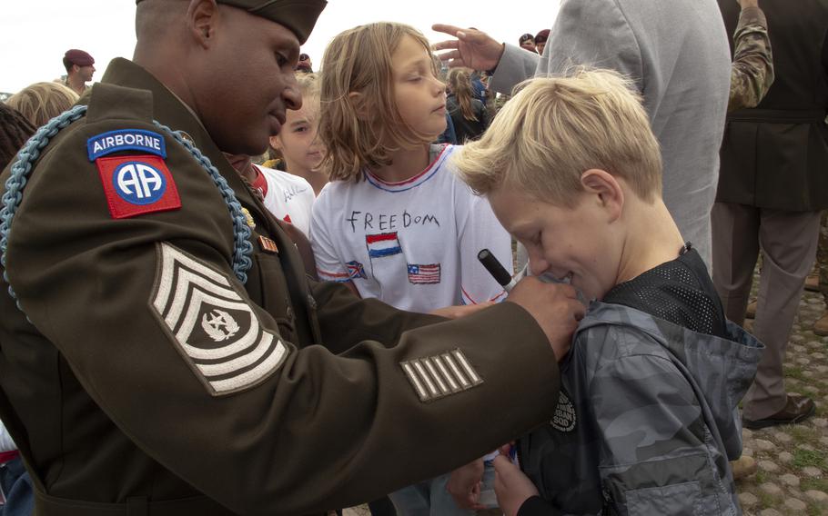 Sgt. Maj. Victor del Valle, left, of the 82nd Airborne Division, signs a Dutch boy's T-shirt at a ceremony in Nijmegen, Netherlands, Sept. 20, 2021, to mark the crossing by U.S. soldiers of the Waal River 77 years earlier.