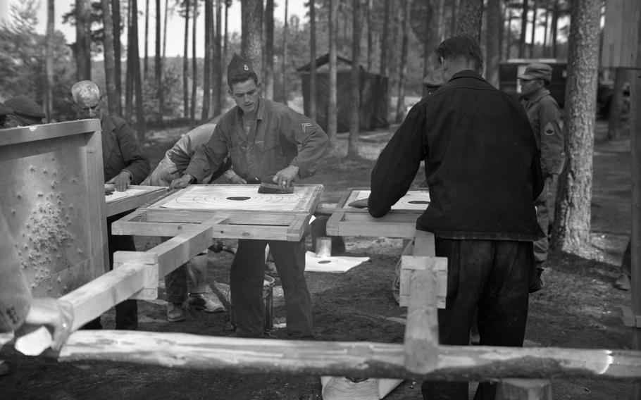 A black and white photo of service members working on something on boards outdoors.