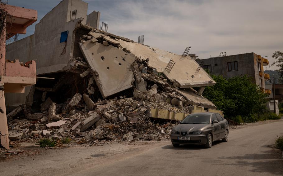 A car drives by a destroyed residential building in Samandag. 