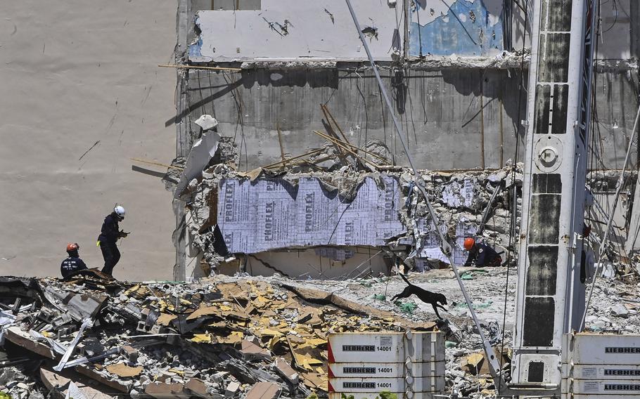 Rescue crew members and their search-and-rescue dog continue to look for survivors Sunday at the collapsed Champlain Towers South condominium building in Surfside, Fla. 