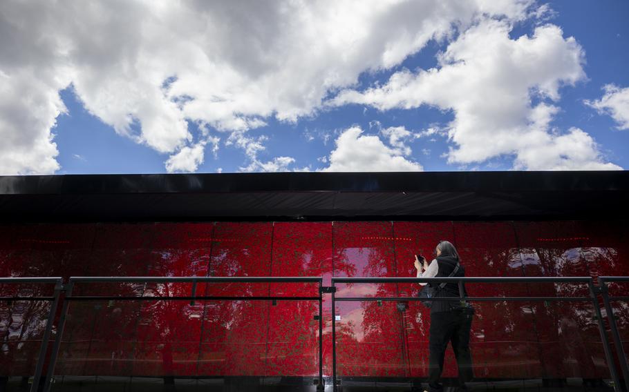 A visitor in the bottom right corner of the image takes a photo of a display that takes up the bottom half of the image; a partly cloudy sky takes up the top half.