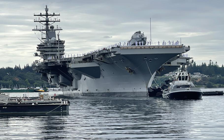 An aircraft carrier is guided into a port by a tugboat.