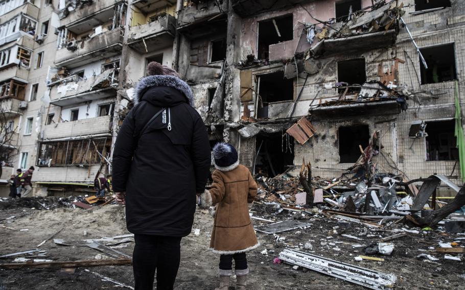 On Feb. 25, two days into the war, people examine a residential building in Kyiv hit by a rocket attack.