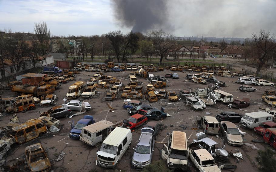 Damaged and burned vehicles are seen at a destroyed part of the Illich Iron & Steel Works Metallurgical Plant, as smoke rises from the Metallurgical Combine Azovstal during heavy fighting, in an area controlled by Russian-backed separatist forces in Mariupol, Ukraine, Monday, April 18, 2022. Mariupol, a strategic port on the Sea of Azov, has been besieged by Russian troops and forces from self-proclaimed separatist areas in eastern Ukraine for more than six weeks. 